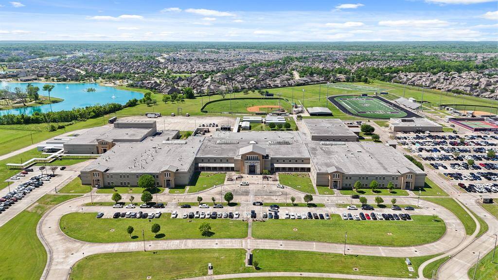This aerial photo showcases a large school complex with extensive sports facilities, including a football field and baseball diamond. It's surrounded by well-maintained green spaces and a nearby residential area, indicating a family-friendly community.
