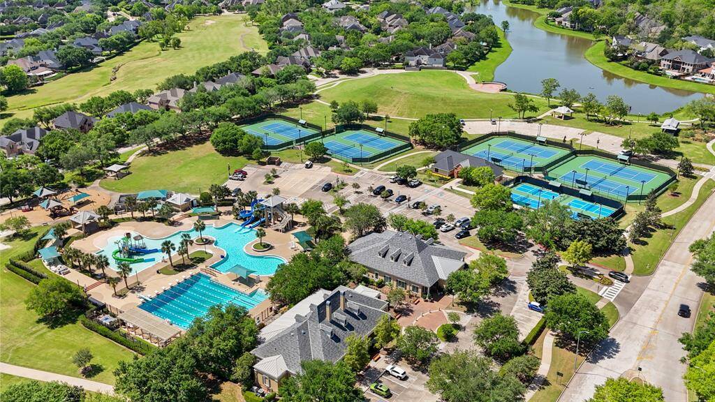 This photo showcases a vibrant residential community featuring a large swimming pool with slides, multiple tennis courts, and a clubhouse. The area is surrounded by lush greenery and a scenic pond, offering recreational and leisure amenities in a picturesque setting. Perfect for active families and those who enjoy outdoor living.