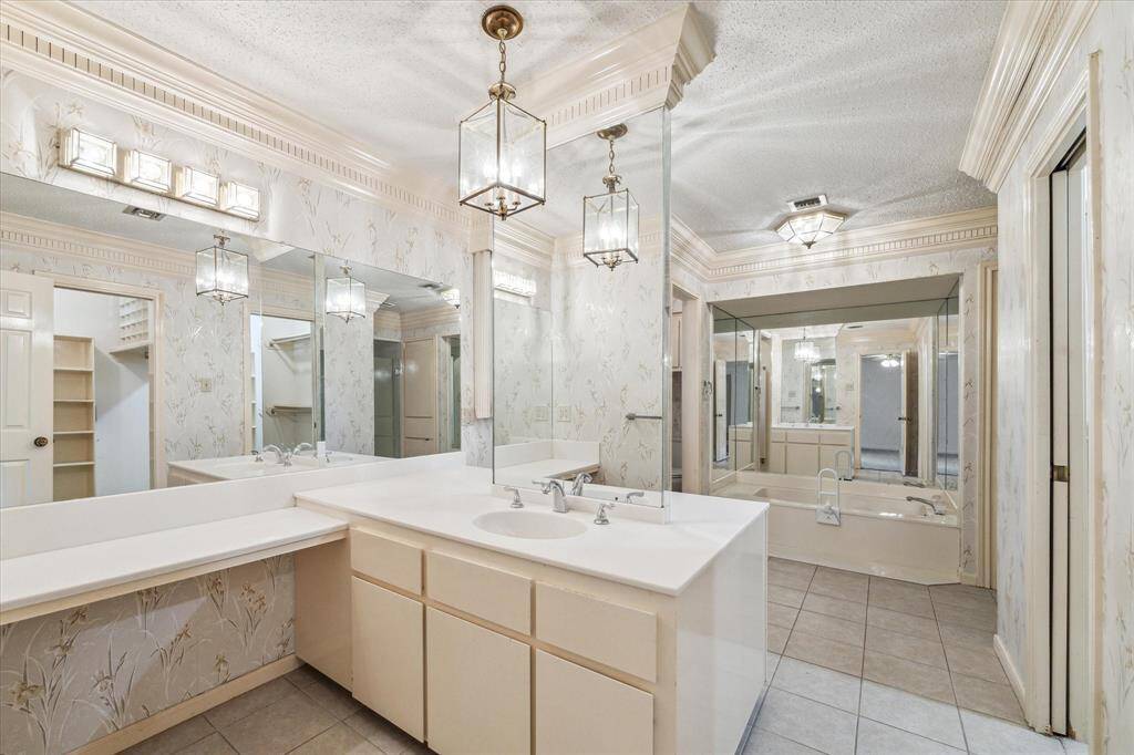 Spacious primary bathroom featuring large mirrors, a double sink vanity, elegant lighting, and a luxurious soaking tub. The room has decorative wallpaper and tiled flooring. Walk in closet and private toilet closet.