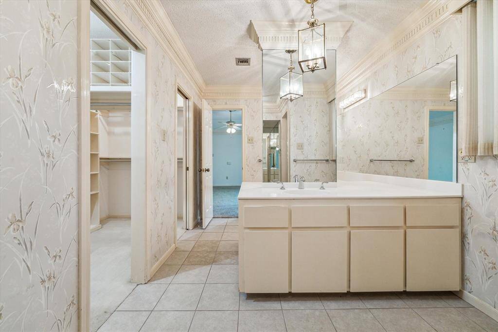 This photo showcases another view of the primary bathroom with a large vanity and mirror, additional pendent light fixtures add light and interest.  Sweet floral wallpaper adds just the right touch.