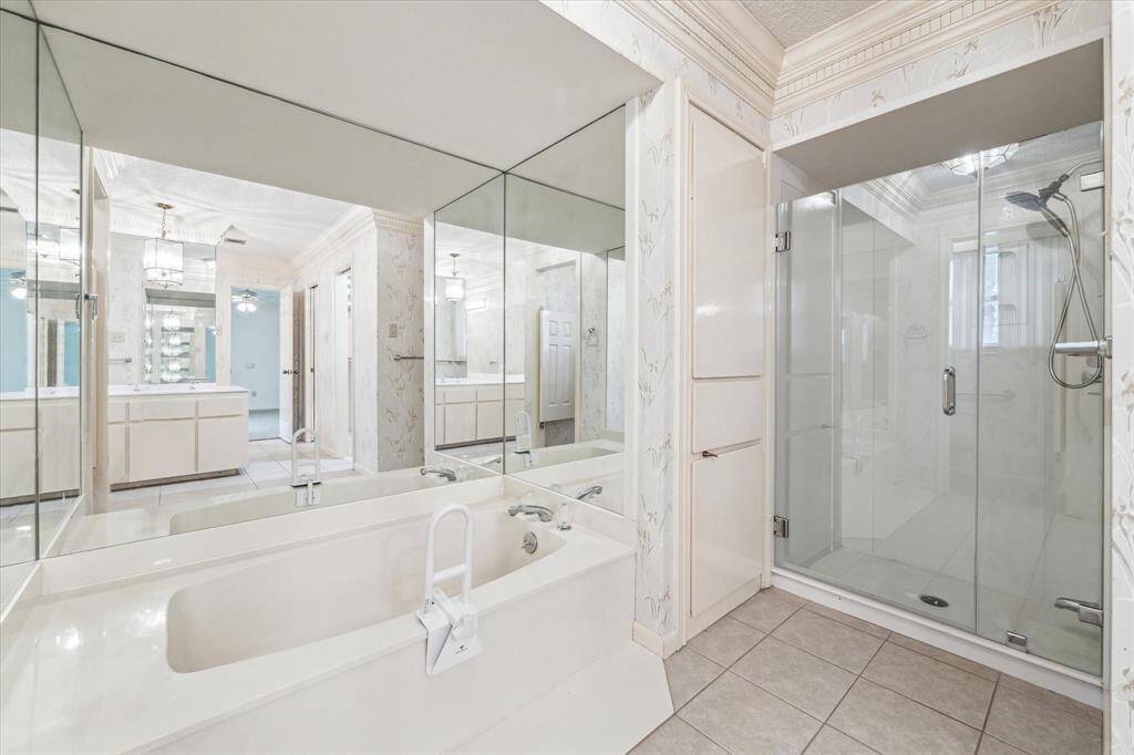 This bathroom features a spacious design with a large soaking tub and a glass-enclosed shower. It includes ample counter space with dual vanities, mirrored walls, and elegant lighting fixtures, creating a bright and luxurious atmosphere.