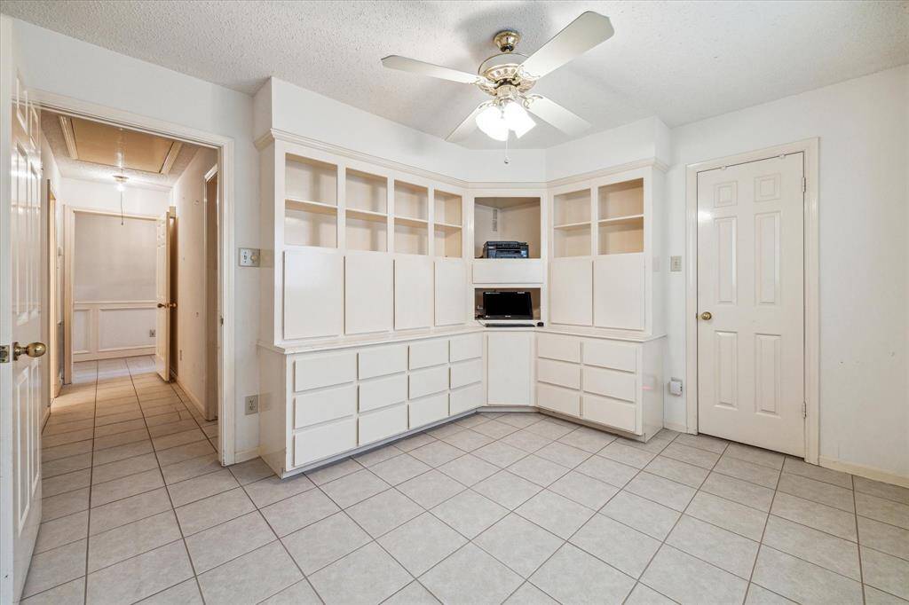This secondary bedroom room features tiled flooring, built-in white cabinetry with open shelving, and a ceiling fan. It offers ample storage and workspace, also ideal for a home office or study area.