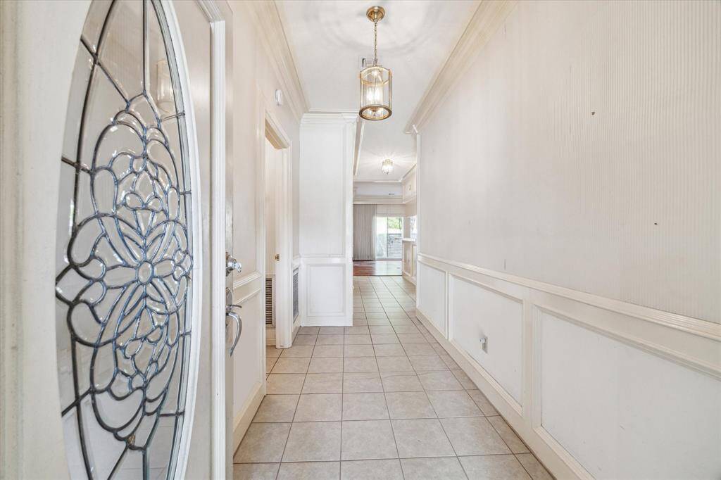 Bright entryway with decorative glass front door, tiled flooring, and elegant wall paneling. Hallway leads to an open living area with ample natural light.
