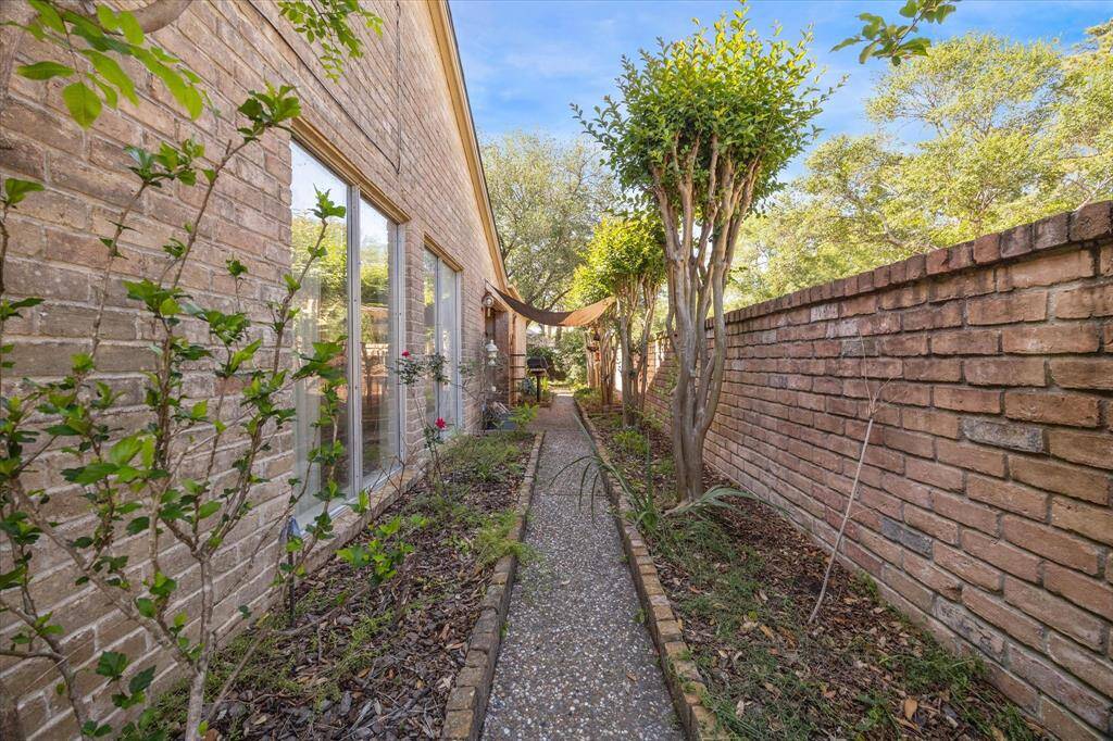 Brick lined garden pathway alongside the house. The path is lined with plants and trees, offering a private outdoor space. A brick wall on the right adds to the secluded feel.
