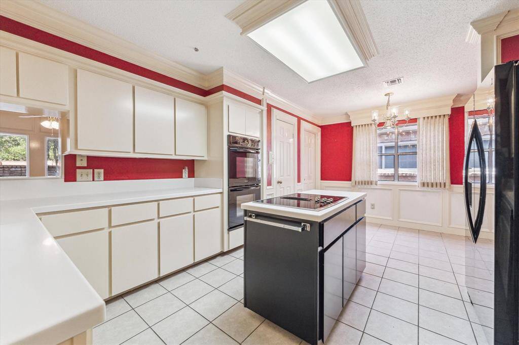 Bright kitchen with white cabinetry and red accent walls. It features a central island cooktop, double ovens, and large windows for natural light. The space is open with tile flooring and elegant lighting fixtures.