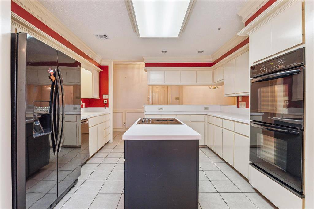 Spacious kitchen with modern appliances, tons of cabinets, storage and ample countertop space. Central island with cooktop. Features a sleek black fridge, double oven, and bright overhead lighting, accented by red walls for a cozy feel.