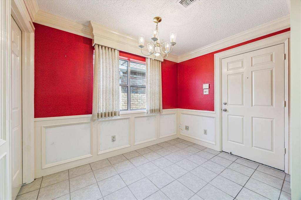 This photo showcases the breakfast area with bold red walls and white wainscoting. It features a window with curtains, a white door, and a decorative chandelier, all set on a tiled floor.