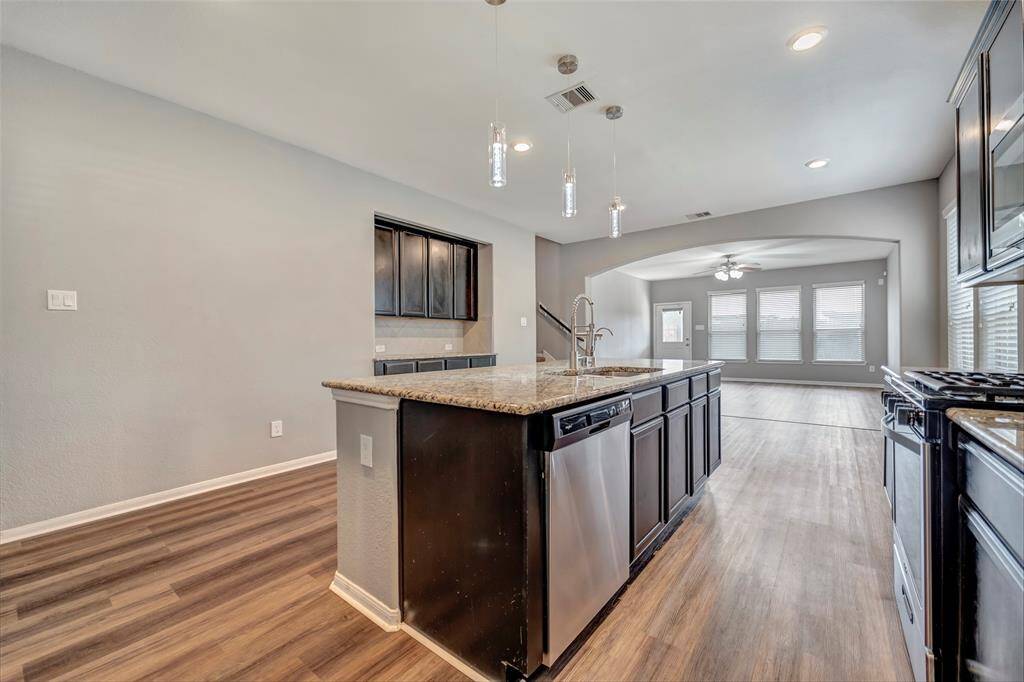 This photo showcases a modern open-concept kitchen and living area with hardwood floors, granite countertops, stainless steel appliances, and ample natural light from multiple windows.
