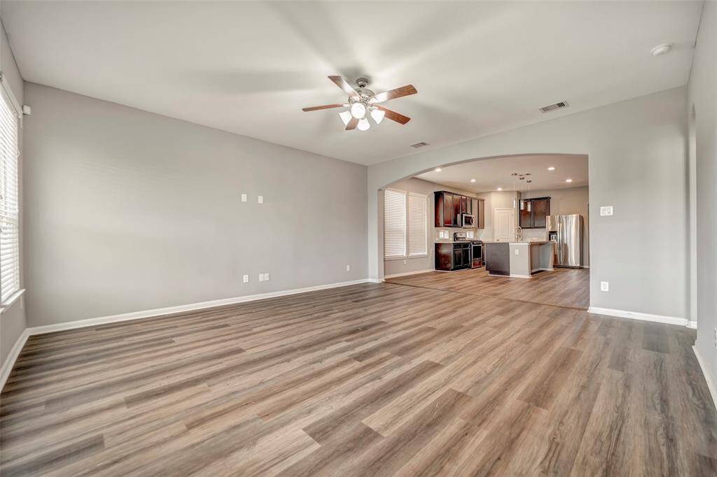 This spacious open-concept living area features modern laminate flooring, a ceiling fan, and flows seamlessly into a well-equipped kitchen with stainless steel appliances and dark wood cabinetry.