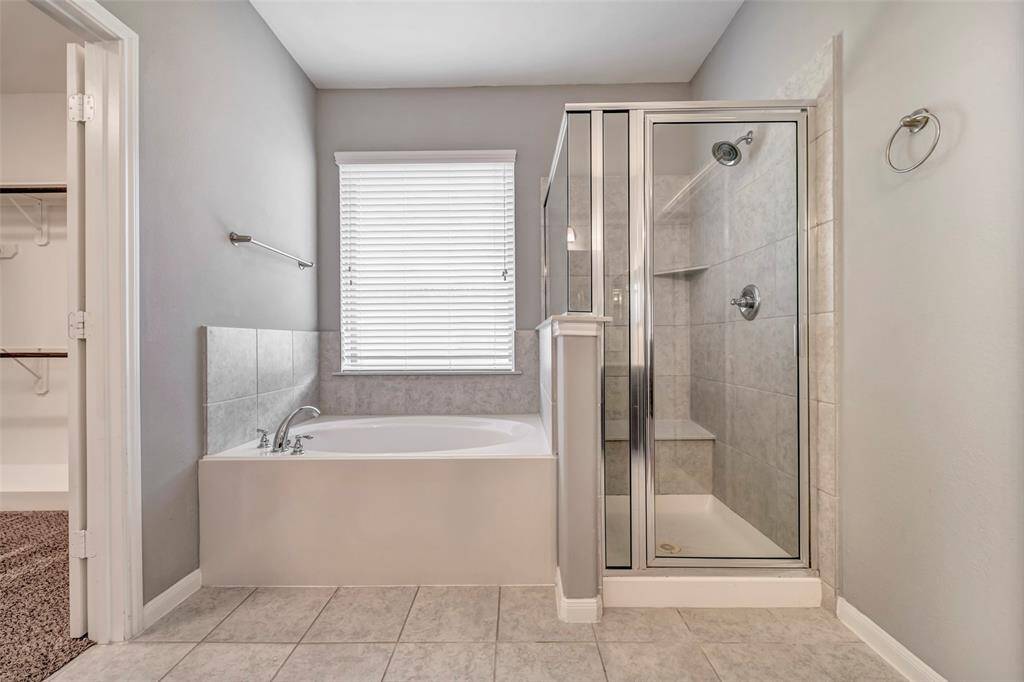 This bathroom features a modern design with a tiled walk-in shower and a separate bathtub. The neutral color palette creates a calm and inviting atmosphere, with a large window providing natural light. Perfect for relaxation and functionality.