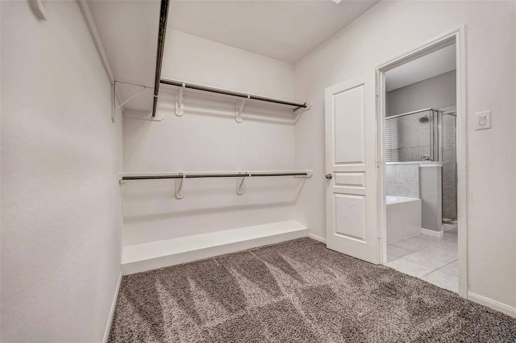 This photo shows a spacious walk-in closet with double hanging rods and shelving, featuring carpeted flooring and an adjacent bathroom with a bathtub and shower.