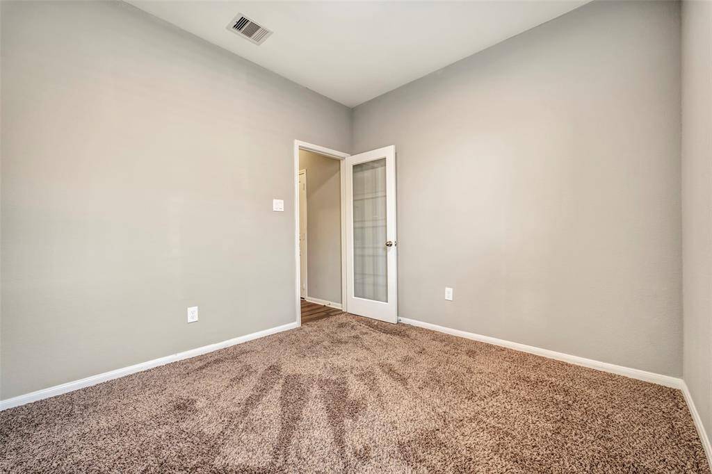 This room features neutral walls, plush carpet, and a glass-panel door leading to another area, offering a cozy and versatile space.