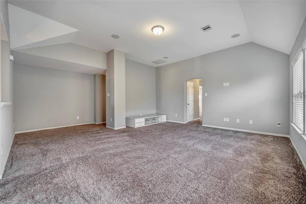 Spacious, carpeted living area with neutral tones. It has an arched doorway leading to another room, and ample natural light from large windows. Ideal for comfortable living and entertainment.
