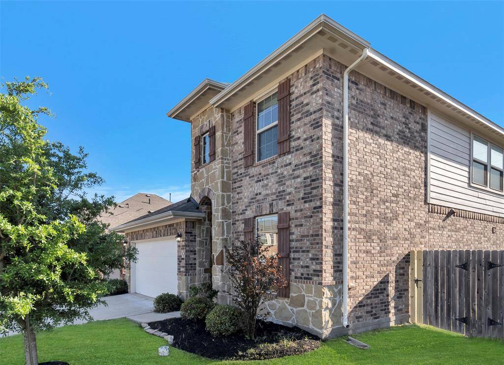 This two-story brick and stone home features a clean exterior with a two-car garage, well-maintained landscaping, and a fenced side yard.