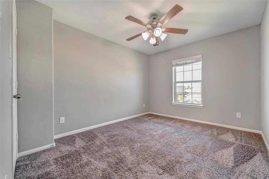 This secondary bed room features neutral gray walls, plush carpet, a ceiling fan with lights, and a window providing natural light, creating a cozy and inviting space.