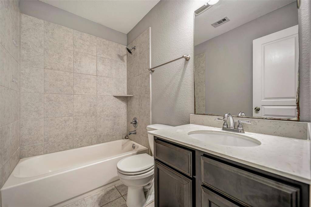 This bathroom features a sleek design with a tiled bathtub/shower combo, modern fixtures, a single vanity with a marble countertop, and a large mirror. Neutral tones create a clean, inviting atmosphere.