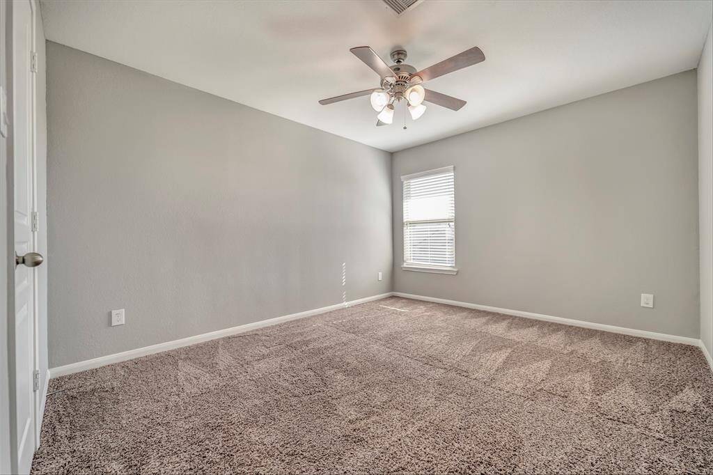 This bed room features neutral gray walls and plush carpet, offering a cozy atmosphere. It includes a ceiling fan with lights and a window for natural light. Ideal for a bedroom or office space.