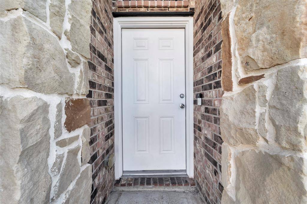 This photo shows a front entryway featuring a white door framed by a combination of brick and stone accents, providing a welcoming and sturdy appearance.