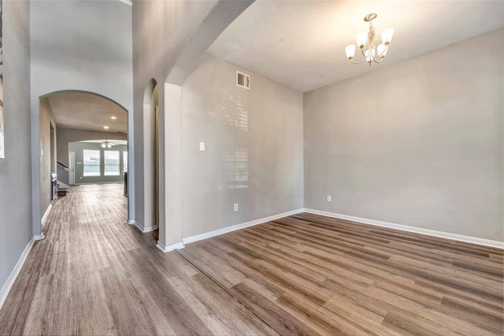 This photo showcases a bright, open hallway with elegant wood flooring and neutral walls. It features an archway leading to a spacious living area with large windows, providing a welcoming and airy atmosphere. A chandelier adds a touch of sophistication to the space.