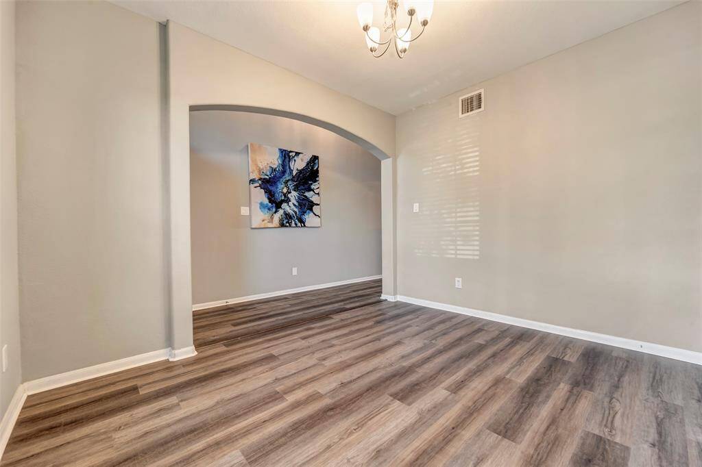 This room features elegant wood-style flooring, neutral walls, and a modern chandelier. An arched entryway leads to another space adorned with a vibrant abstract painting. Perfect for a cozy yet stylish setting.
