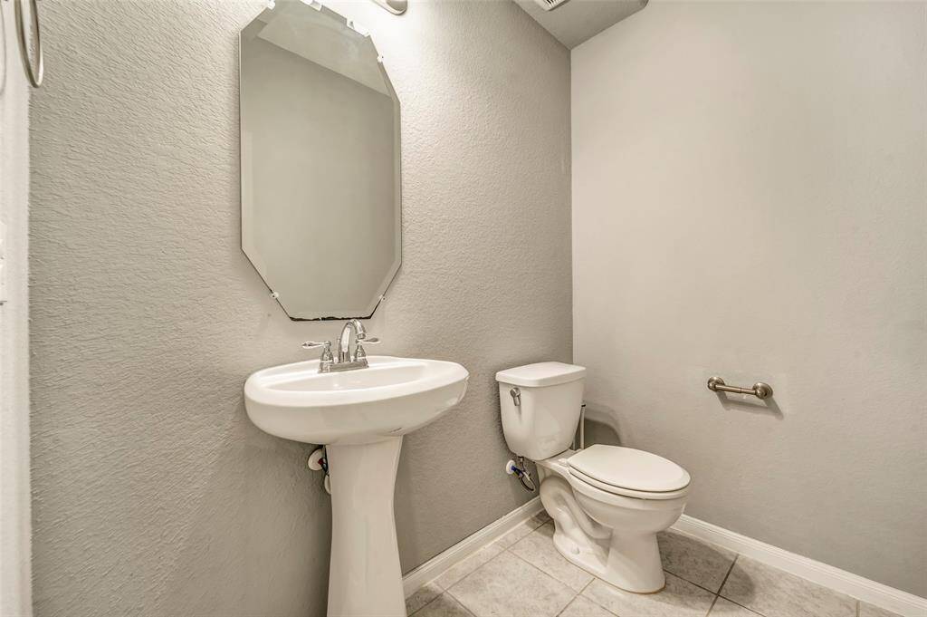 This is a compact, clean bathroom featuring a pedestal sink, a large mirror, and a standard toilet. The light-colored walls and tiled floor create a bright, simple space.