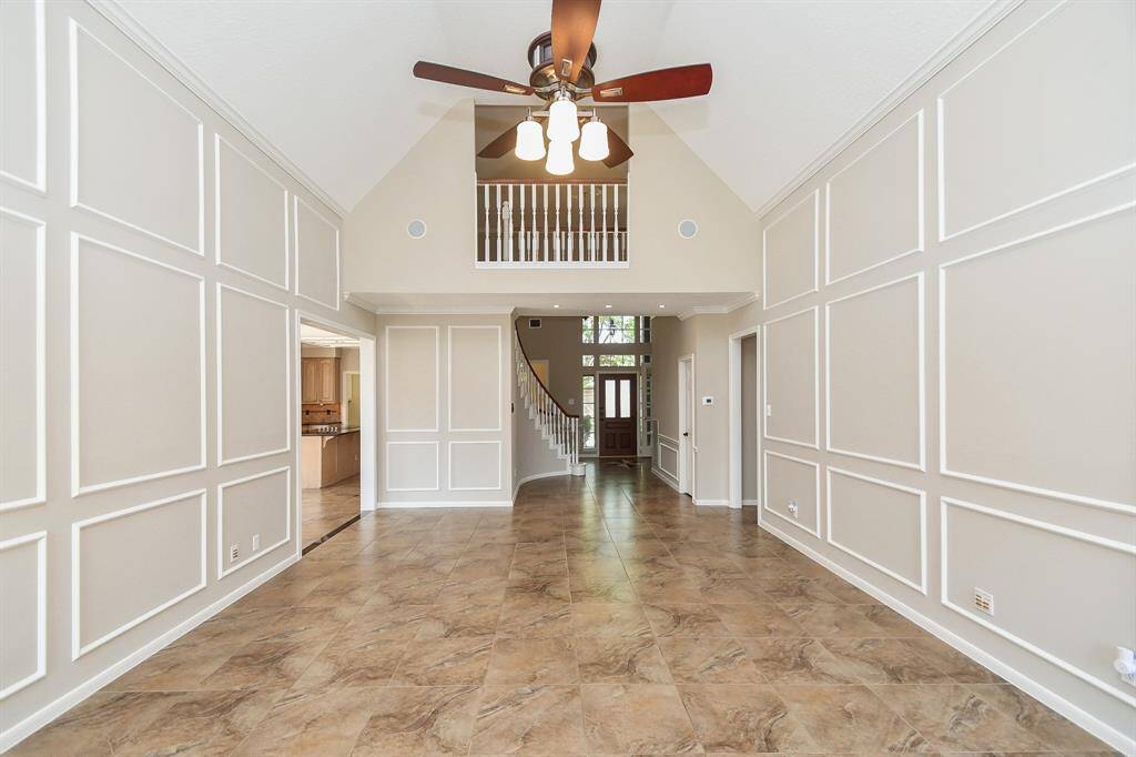 This elegant spacious living area features high vaulted ceilings. It opens up to a staircase and a view of the front door, providing a bright and inviting entryway. The tile flooring adds a touch of sophistication.