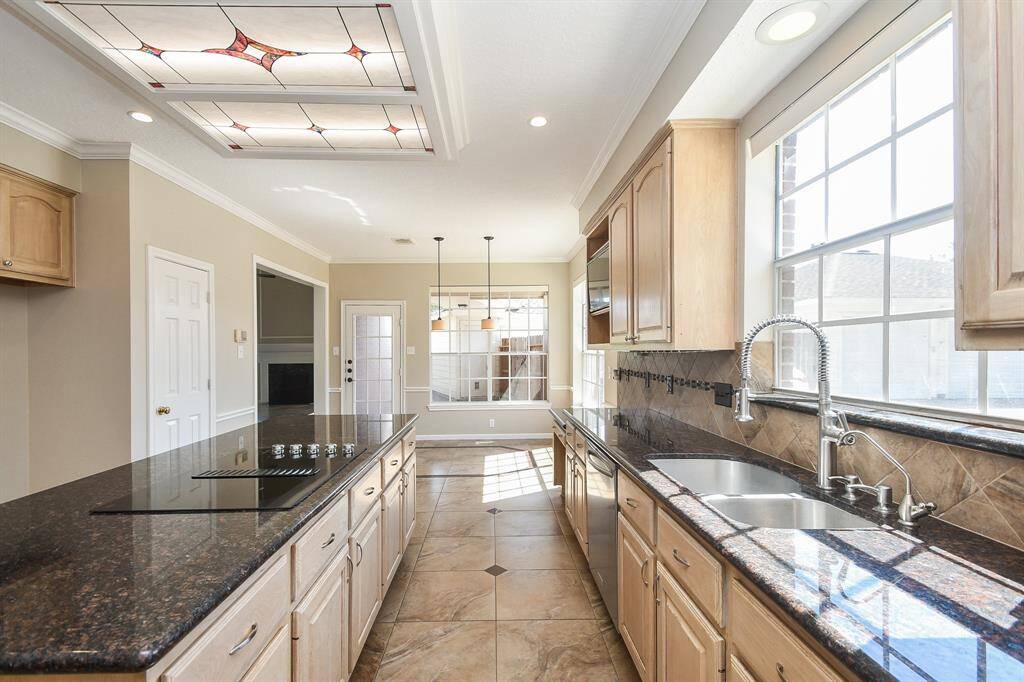 This kitchen features granite countertops, ample natural light from large windows, and wooden cabinetry. The modern design includes a sleek island cooktop and a double sink, making it both functional and stylish.