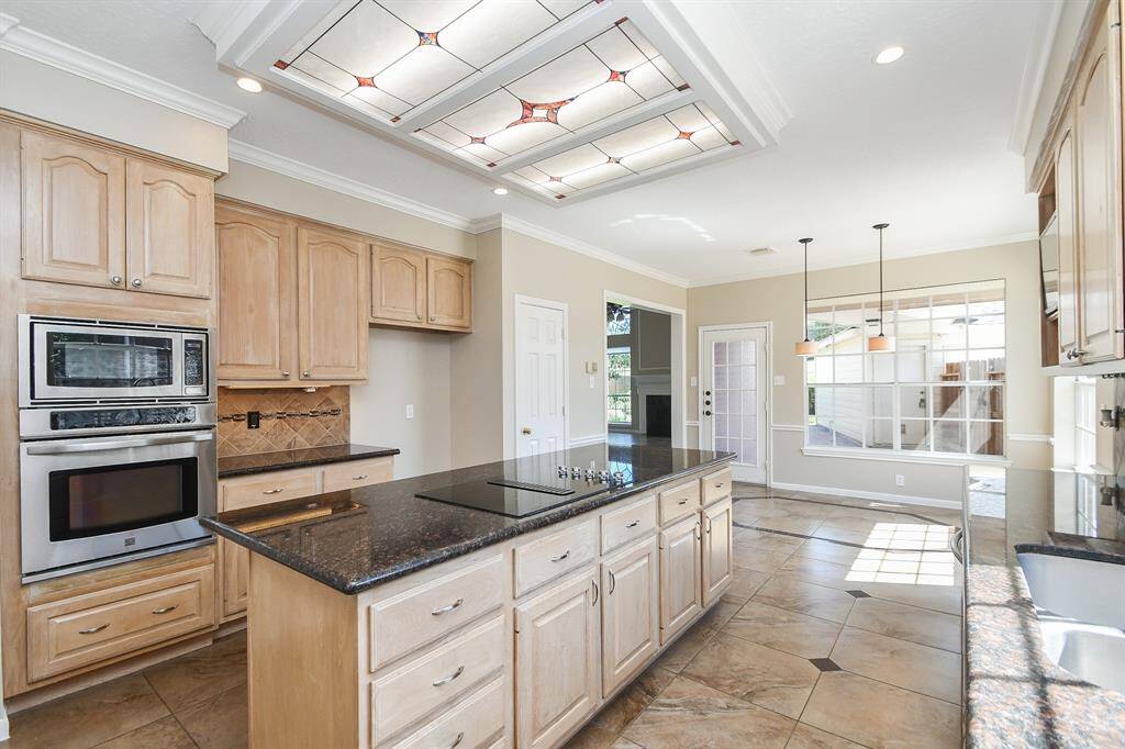 Spacious kitchen featuring light wood cabinetry, granite countertops, and a large central island. It includes a built-in oven, ample natural light from large windows, and stylish ceiling lights. Perfect for cooking and entertaining.