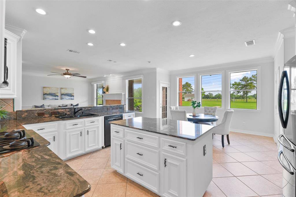 Fine finishes in the kitchen include exotic granite countertops with deep veining, a ceramic tile backsplash, recessed lighting, tile floors, and an abundance of freshly painted cabinetry for storage.