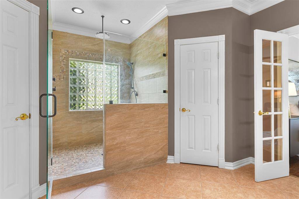 Step into this extra large shower with a rainfall showerhead in addition to a handheld showerhead, a lovely tile surround with mosaic tile detailing, a glass tile window to allow for natural light, and a seamless glass door.
