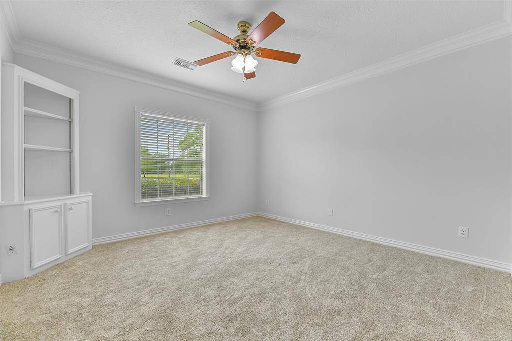 The first of two secondary bedrooms that are located on the first floor offers a lighted ceiling fan, fresh neutral paint trimmed with crown molding, a built-in corner cabinet, brand new plush carpet, a walk-in closet with built-in dresser, and a front-facing window shaded by 2-inch blinds.