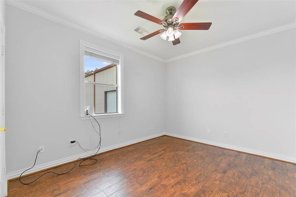 The remaining secondary bedroom on the first floor offers luxury vinyl plank flooring, neutral paint, crown molding, a walk-in closet with a built-in dresser, and a rear-facing window shaded by 2-inch blinds. There is a half bathroom just outside of the room.