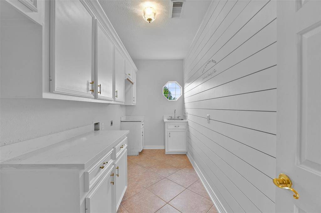 The utility room is especially noteworthy, offering a wall of cabinetry complete with a hanging rack, a utility sink, a space for a bonus refrigerator, quartz countertops, tile flooring, an octagonal window, and a stylish shiplap wall.