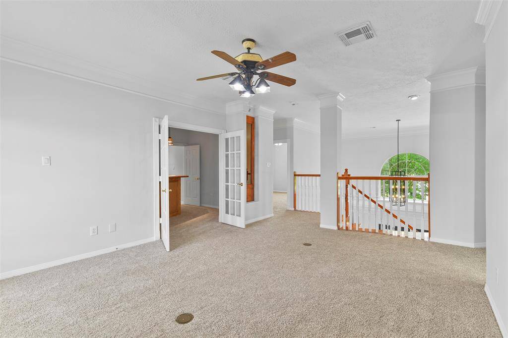 Head up the sweeping Cinderella-inspired staircase with wood treads to this second-floor living space that offers a lighted ceiling fan, fresh neutral paint, triple crown molding, a built-in curio cabinet, plush new carpet, & French doors to a balcony as well as a gameroom.