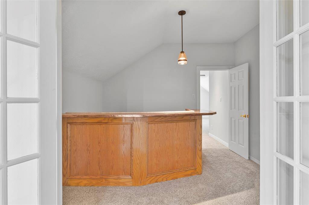 French doors lead from the second-floor living space into this bar area that adjoins the game room on the other side. Notice the solid wood built-in bar with a stylish copper countertop, a beverage fridge, bartop seating space, and a pendant light.