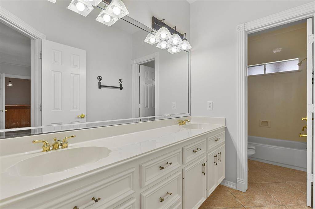 This bathroom services the second floor and it boasts a lengthy cultured marble countertop with dual basin sinks, freshly painted cabinetry, a beveled frame mirror, tile floors, and a combination bathtub and shower with a cultured marble surround.