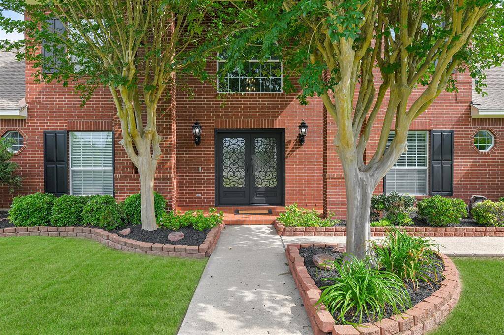 Access the house from either the sidewalk from the street beyond a three-tiered trickling water fountain, or via the sidewalk from the driveway and you'll pass a flagpole and freshly mulched established landscape beds before you arrive at the covered front porch with double doors.