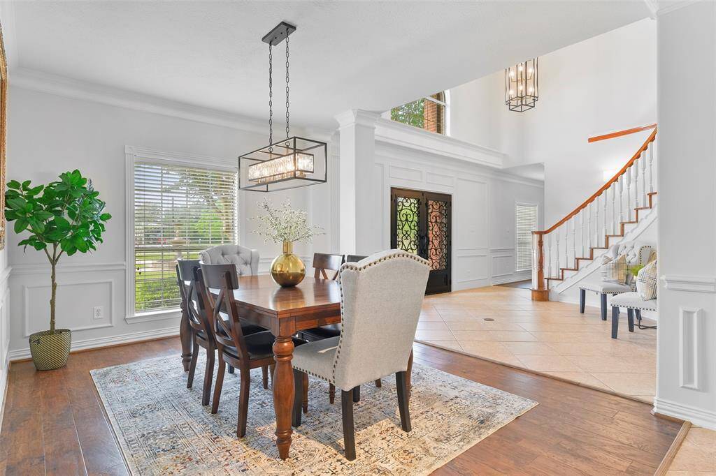 The impressive foyer makes way to an elegant formal dining room complete with wood-look luxury vinyl plank flooring, fresh neutral paint, ornate moldings, a stylish black, gold, & crystal caged chandelier, and a front-facing window shaded by 2-inch blinds.