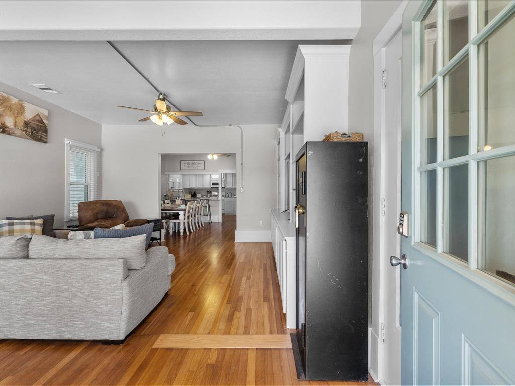 This photo showcases an open-concept living area with hardwood floors, a ceiling fan, and built-in shelves. It leads into a dining area and kitchen, creating a spacious, connected feel. Natural light streams in through multiple windows, enhancing the welcoming atmosphere.