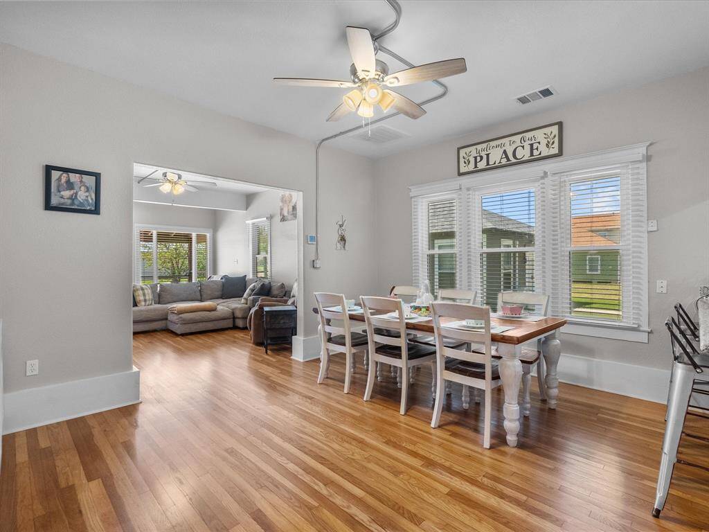 This photo showcases a bright, open dining area with hardwood floors and a ceiling fan. It connects to a cozy living room featuring large windows and a sectional sofa, creating a welcoming atmosphere.