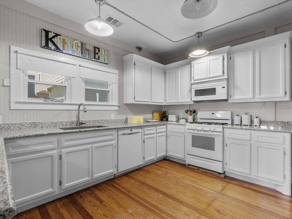 This kitchen features white cabinetry, granite countertops, and stainless steel appliances, complemented by warm hardwood floors and ample natural light from large windows.
