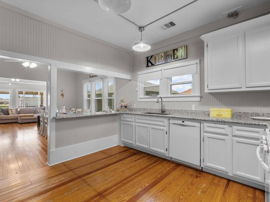 Bright kitchen with white cabinets, granite countertops, and hardwood floors. Open layout connects to a living area with ample natural light through large windows. Ideal for entertaining.