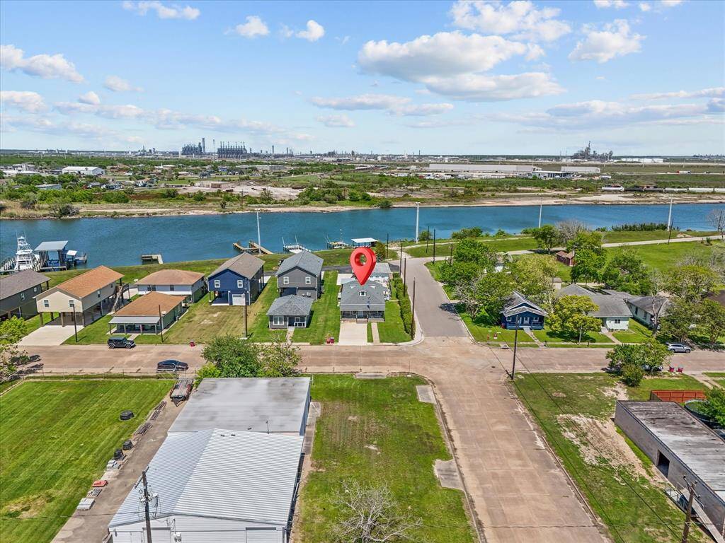 This aerial photo showcases a charming neighborhood with a row of houses on the river. The highlighted property is centrally located, offering scenic water views and a spacious yard. The area is tranquil, with nearby greenery and easy access to the water.