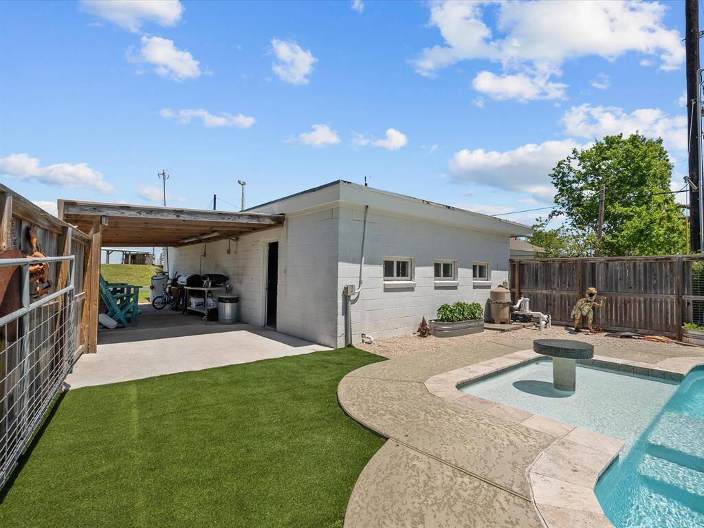 This backyard features a covered patio area, artificial turf, and a small pool with a fountain. It's enclosed by a wooden fence, providing privacy, and has a concrete path for easy access.