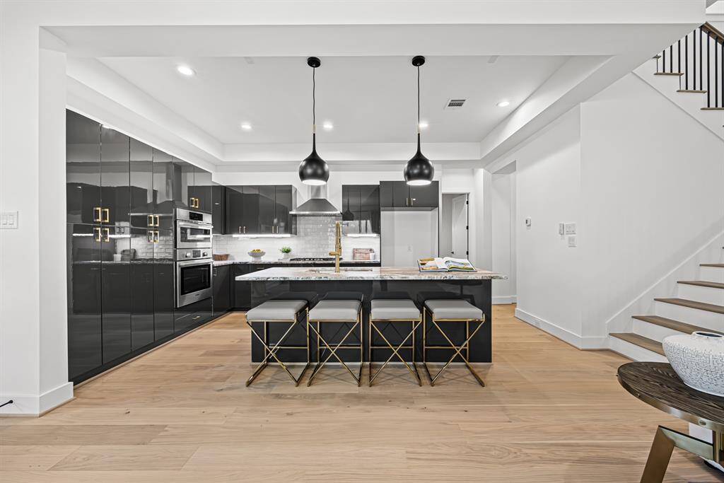 This modern kitchen features sleek black cabinetry, high-end appliances, and a spacious island with stylish bar stools. The open layout and hardwood floors offer a bright, inviting space, ideal for both cooking and entertaining.