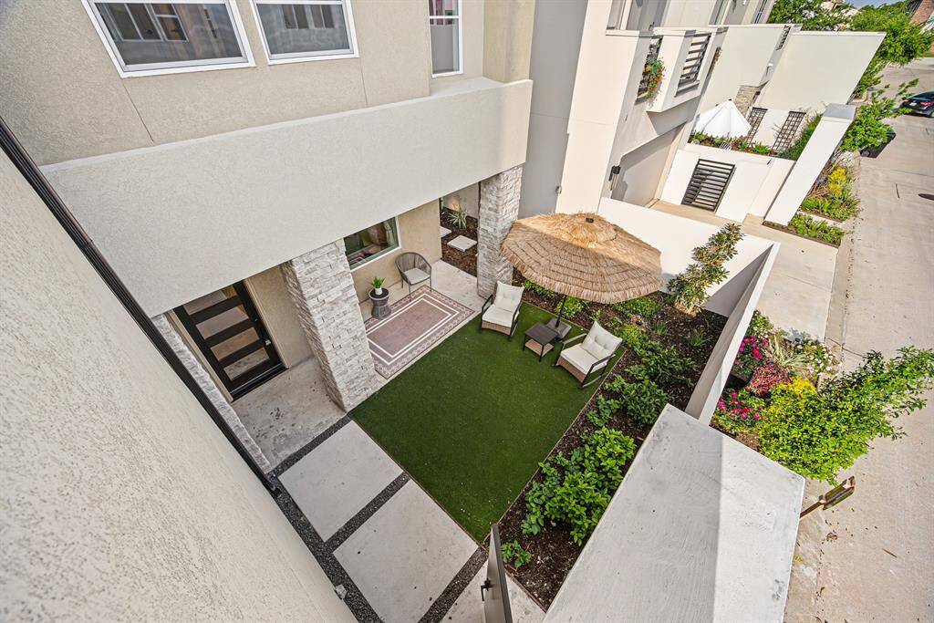 This photo showcases a modern courtyard with artificial grass, a cozy seating area under a large patio umbrella, and surrounding greenery, offering a private outdoor space ideal for relaxation and entertaining.