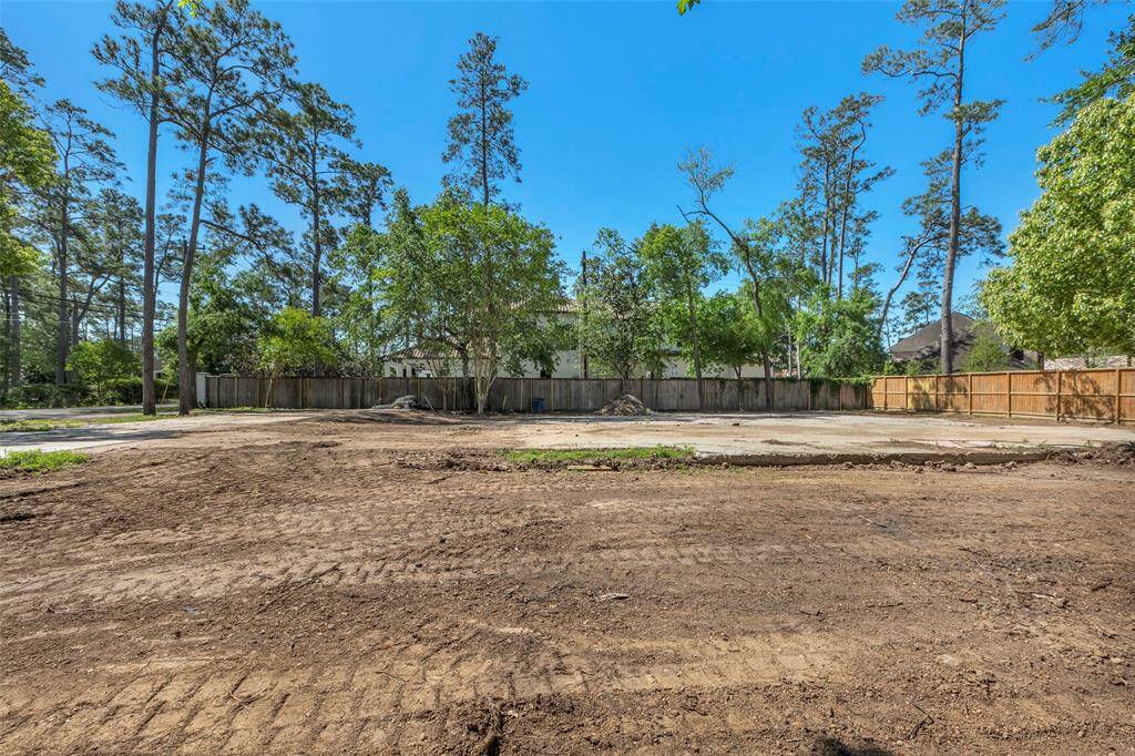This photo shows a spacious, cleared lot surrounded by mature trees, with a wooden fence at the back. It's located in a quiet, residential area with neighboring homes visible, offering a serene setting with ample  potential for development.