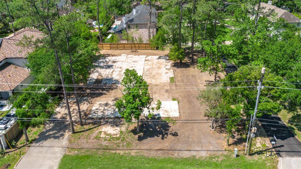 This photo shows a spacious, cleared lot surrounded by mature trees, with a wooden fence at the back. It's located in a quiet, residential area with neighboring homes visible, offering a serene setting with ample  potential for development.
