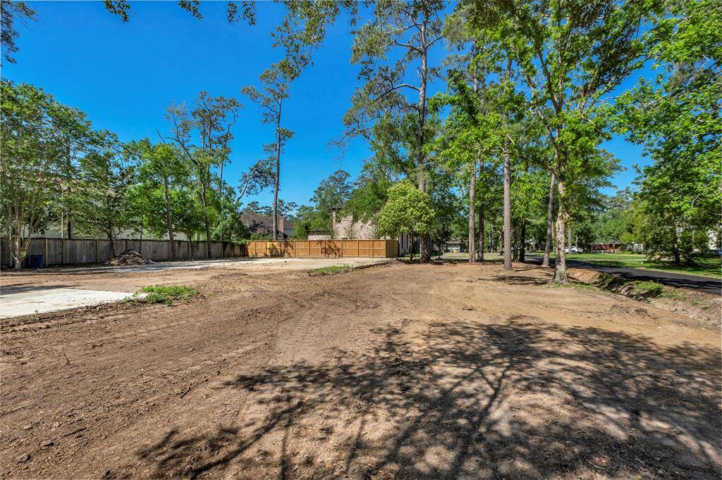 This photo shows a spacious, cleared lot surrounded by mature trees, with a wooden fence at the back. It's located in a quiet, residential area with neighboring homes visible, offering a serene setting with ample  potential for development.