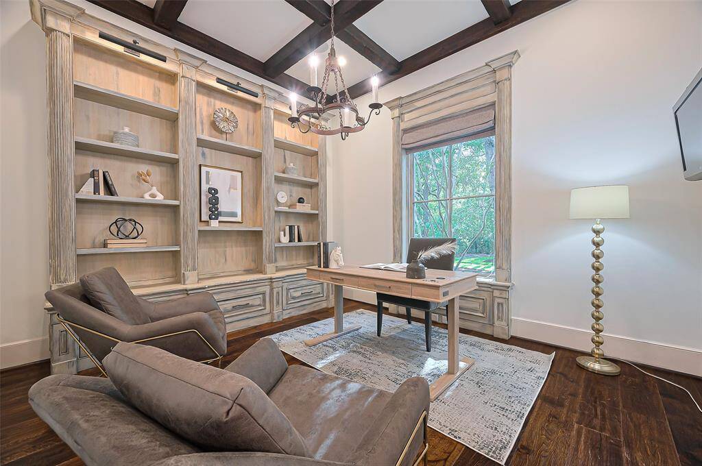The stylish home office with high ceilings, featuring a chandelier, built-in bookshelves, and sleek furniture. The space has a warm, inviting atmosphere with elegant decor and a polished wooden floor.